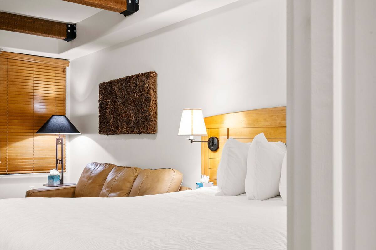 Een hotelkamer met een bed, een houten hoofdbord, een wandlamp, een nachtkastje met een lamp, en een decoratief wandobject met reliëf.
