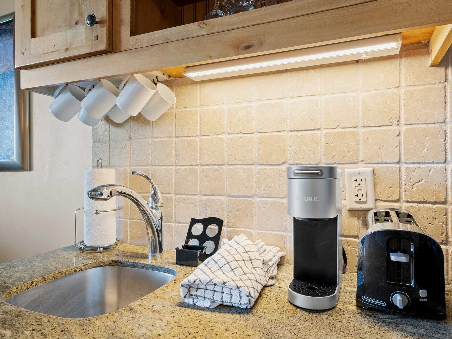 Une cuisine dotée d’un plan de travail en granit, d’un évier en acier inoxydable, d’une machine à café, d’un grille-pain et d’une serviette.
