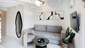 A modern living room with a grey sofa, a round glass coffee table, a large mirror, and three abstract wall art pieces. - N&G Deluxe Maisonette (Lefkada)
