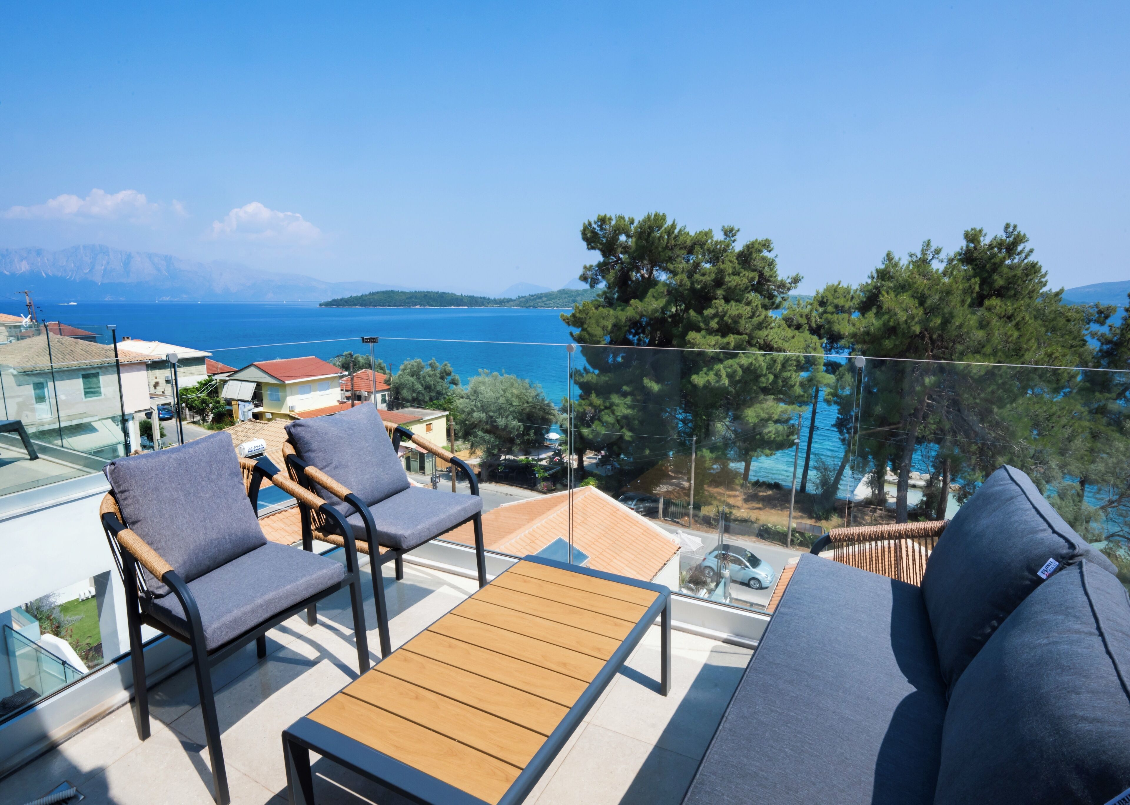 Ein Balkon mit Gartenmöbeln, freier Blick auf das Meer und eine ferne Bergkette.