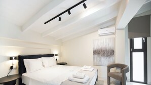 A modern hotel room with a large bed, a round side table, a chair, and a wall-mounted air conditioning unit. - N&G Deluxe Maisonette (Lefkada)
