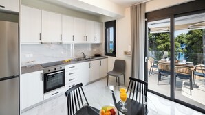 A modern kitchen with white cabinets, a black countertop, and a dining area with a glass table and chairs. - N&G Deluxe Maisonette (Lefkada)