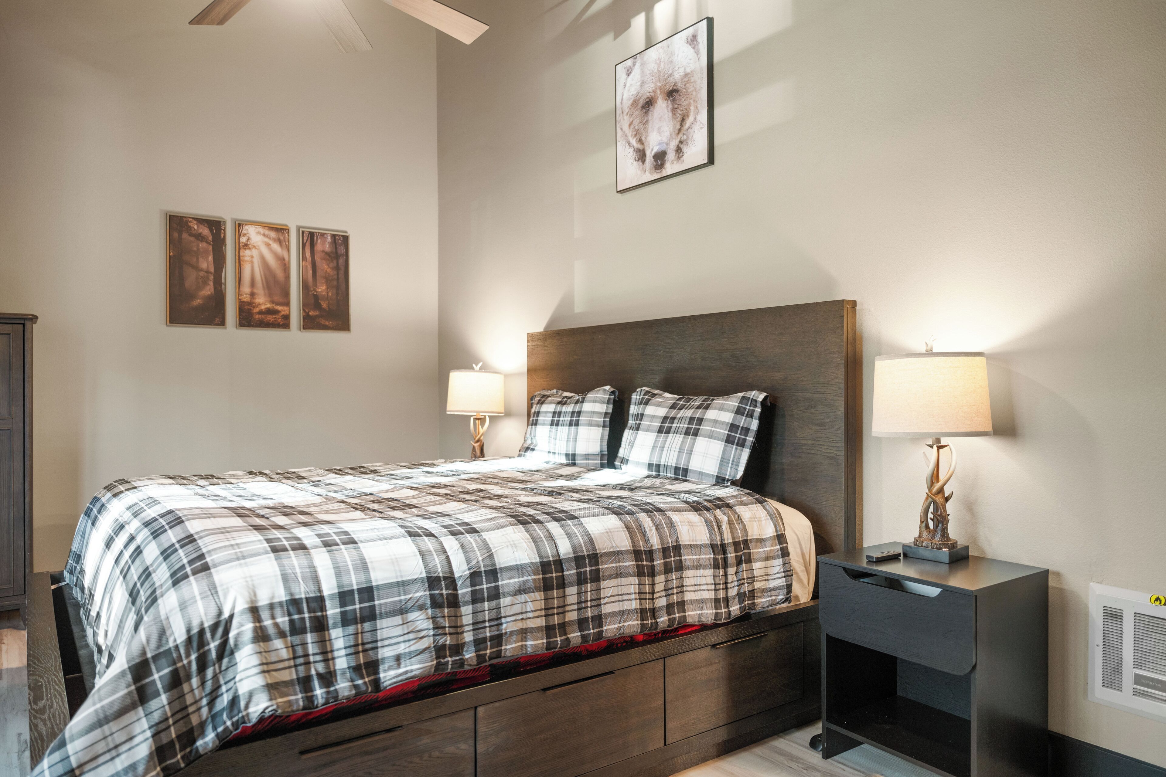 A bedroom with a bed, two bedside tables, and three wall-mounted pictures.