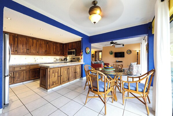 A kitchen with wooden cabinets, a dining area with wicker chairs, and a ceiling fan.
