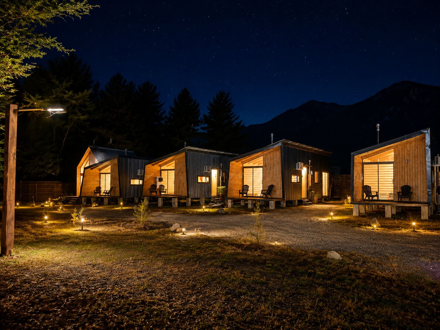 A row of cabins with large windows, outdoor seating, and a starry night sky.