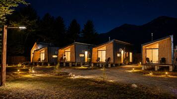 A row of cabins with large windows, outdoor seating, and a starry night sky.