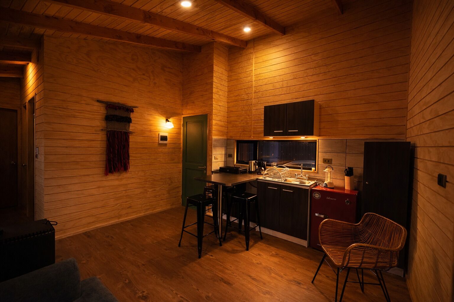 A compact kitchen with wooden walls, a small dining area, and a bar stool.