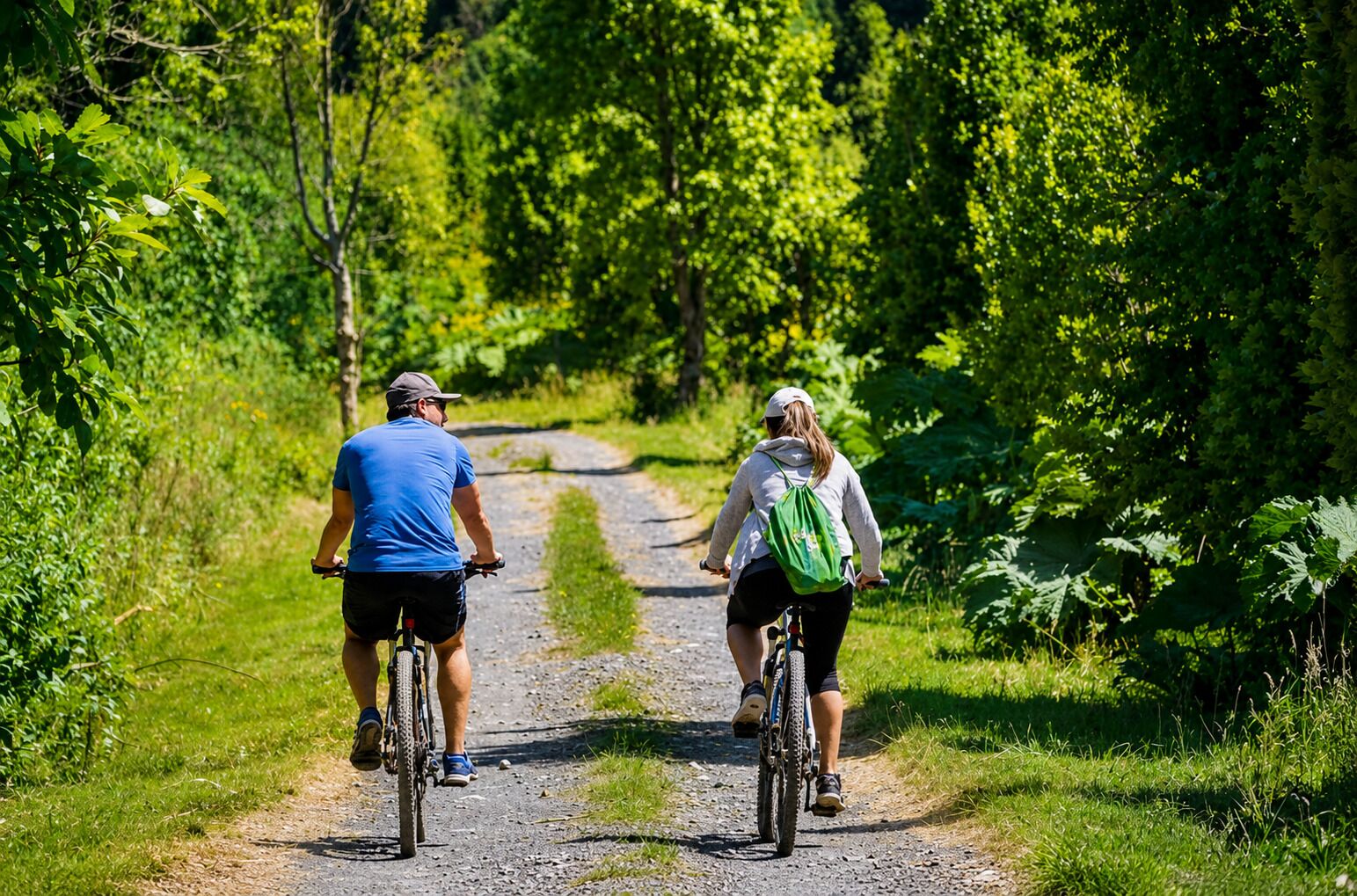 Two people riding bicycles on a gravel path surrounded by greenery.