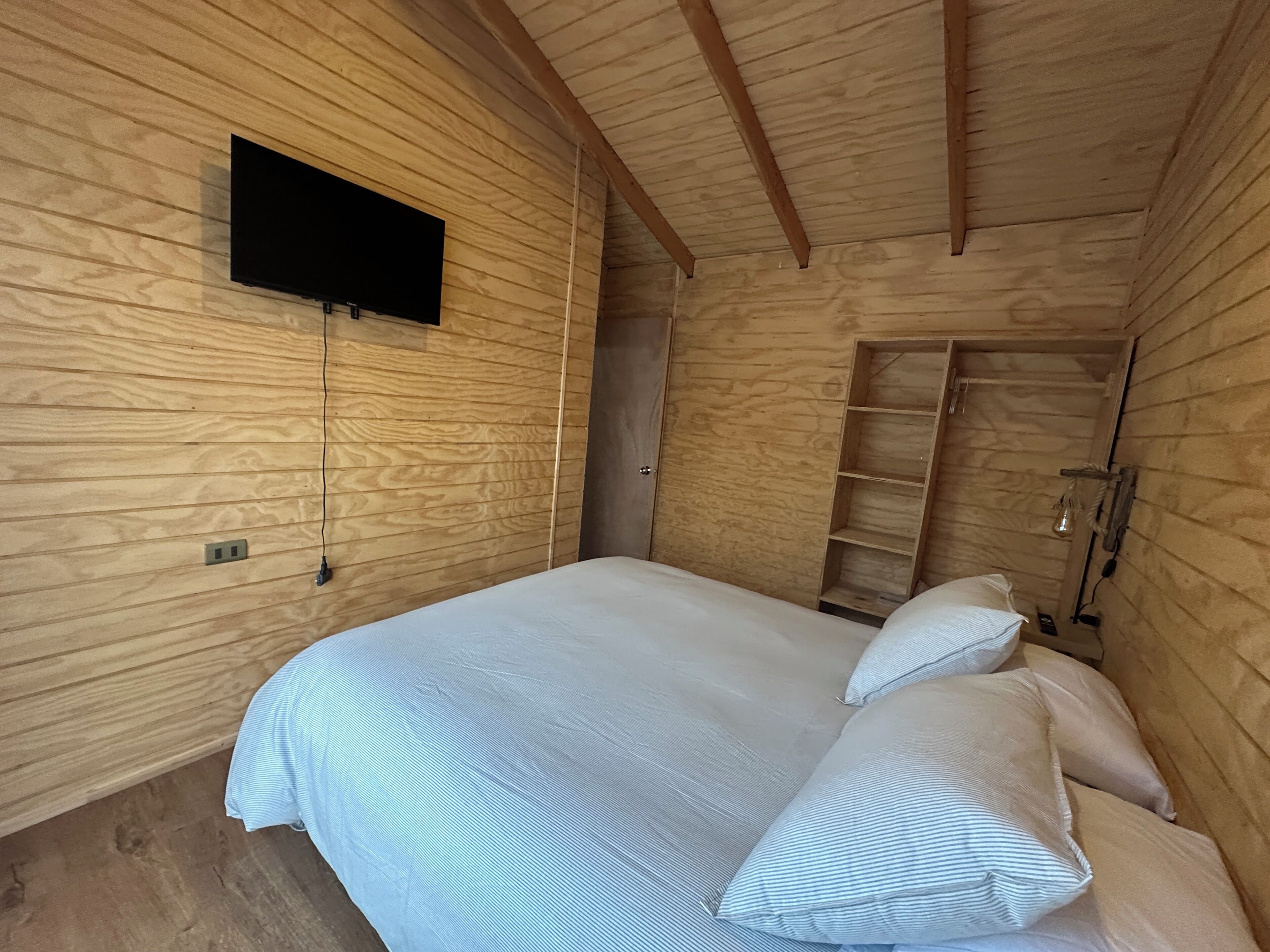 Una habitación de madera con una cama, un televisor en la pared y un armario de madera.