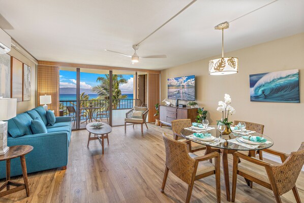 Un salón espacioso con vistas al océano, una mesa de comedor preparada para cuatro personas y un sofá con cojines azules.