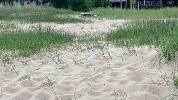 Una playa arenosa con escasa hierba y una pequeña construcción de madera al fondo.