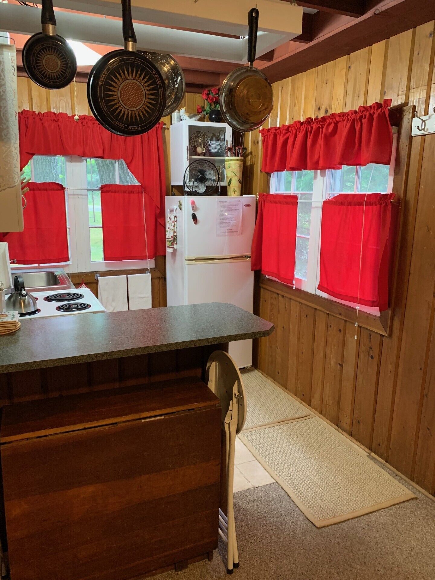 A compact kitchen with wooden walls, a white refrigerator, a stove, and red curtains.
