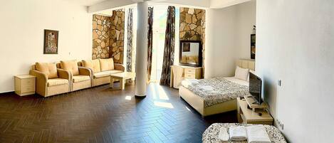 A hotel room with a herringbone floor, a sofa set, a bed, a TV, and a stone accent wall.