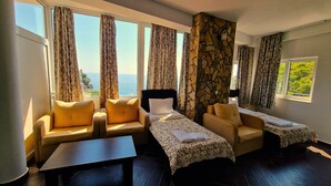 A hotel room with a sofa, two single beds, a small table, and large windows with curtains. - AZURA BAY HOTEL (Dobra Voda)