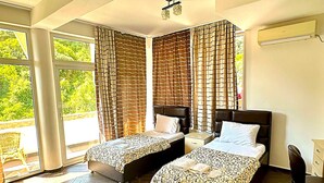 A hotel room with two beds, a large window, and a view of greenery outside. - AZURA BAY HOTEL (Dobra Voda)
