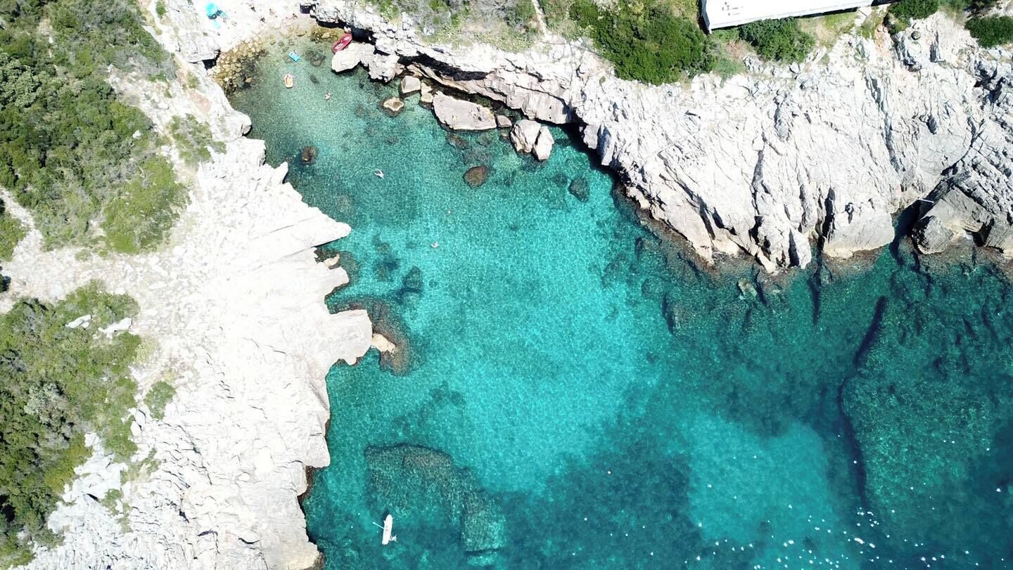 A coastal landscape with clear turquoise waters, rocky cliffs, and sparse vegetation.