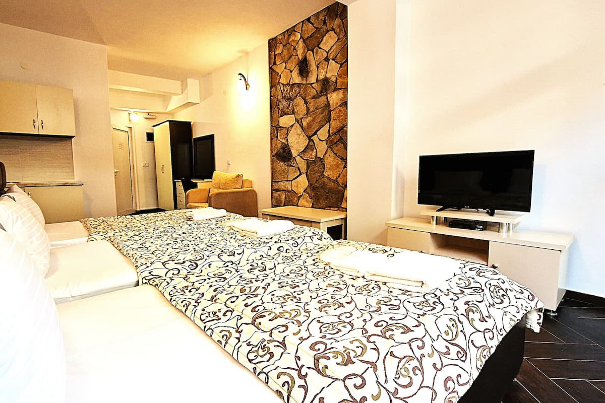 Una habitación de hotel con cama, televisión, pared de piedra y un pequeño rincón de descanso.