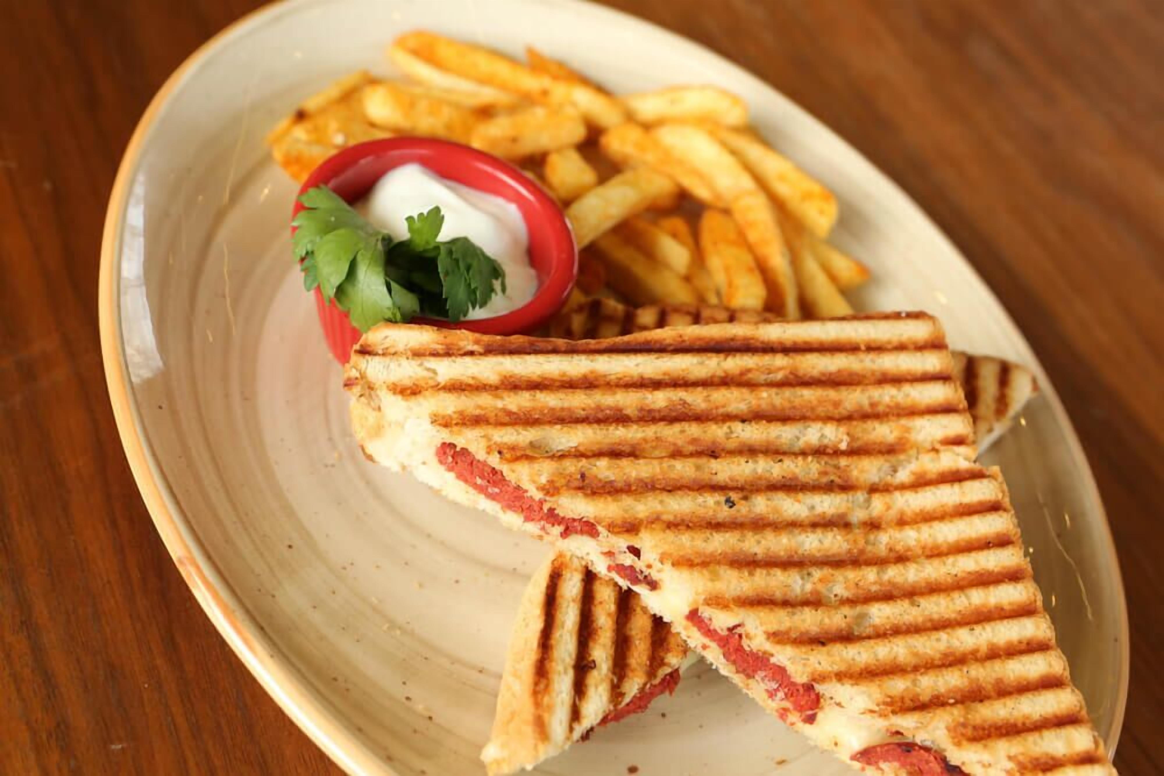 Un sandwich grillé, accompagné de frites et d’un petit bol de sauce, le tout servi sur une assiette.