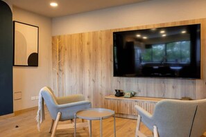 A modern living room with two light-colored armchairs, a small round table, a flat-screen TV mounted on a wooden wall, and a vintage telephone on a wooden console. - Digital Nomad Paradise 2BR unit Steps from Manila (Medellín)