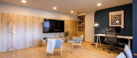 Un espacio de oficina moderno con suelo de madera, un escritorio, dos sillas, un televisor y estanterías con adornos.