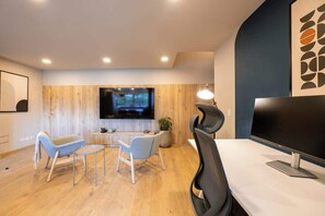 A modern office space with a large TV, two light blue chairs, a desk, and a potted plant.