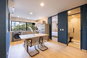 A modern kitchen with a dining area, a washing machine, and a view of the city.