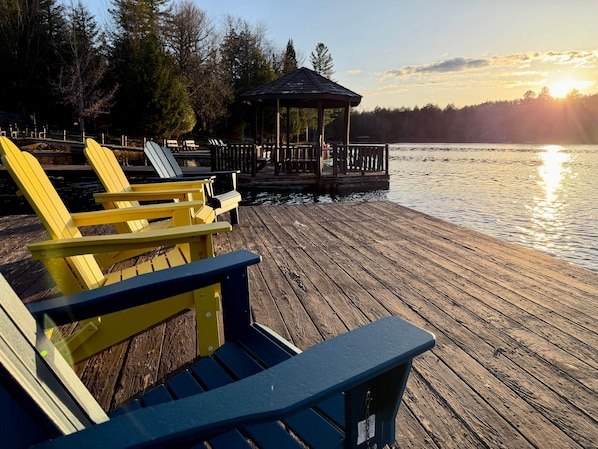 A wooden dock with chairs, a gazebo, and a lake.