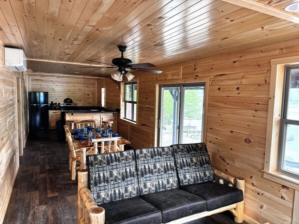 A wooden cabin interior with a dining area, sofa, and kitchen.