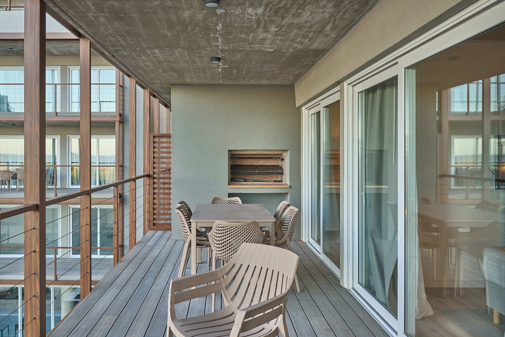 A balcony with a wooden table and chairs, a built-in bench, and large sliding glass doors.
