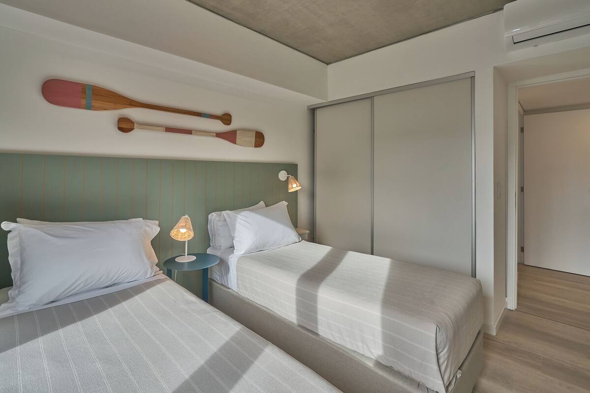 A hotel room with two beds, a wooden paddle wall decoration, a bedside lamp, and a sliding door.