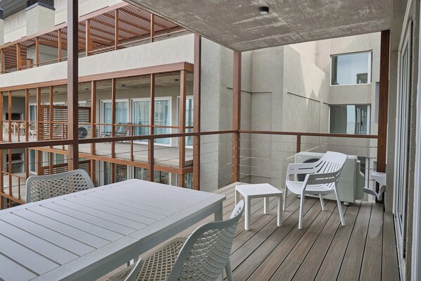 A modern outdoor balcony with a table and chairs, a grill, and a view of the building's interior. - Almarena La Reserva (Costa del Este)