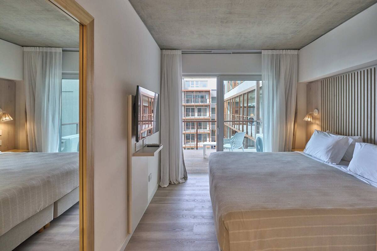 A modern hotel room with a large bed, a TV, and a balcony with a view of the city.