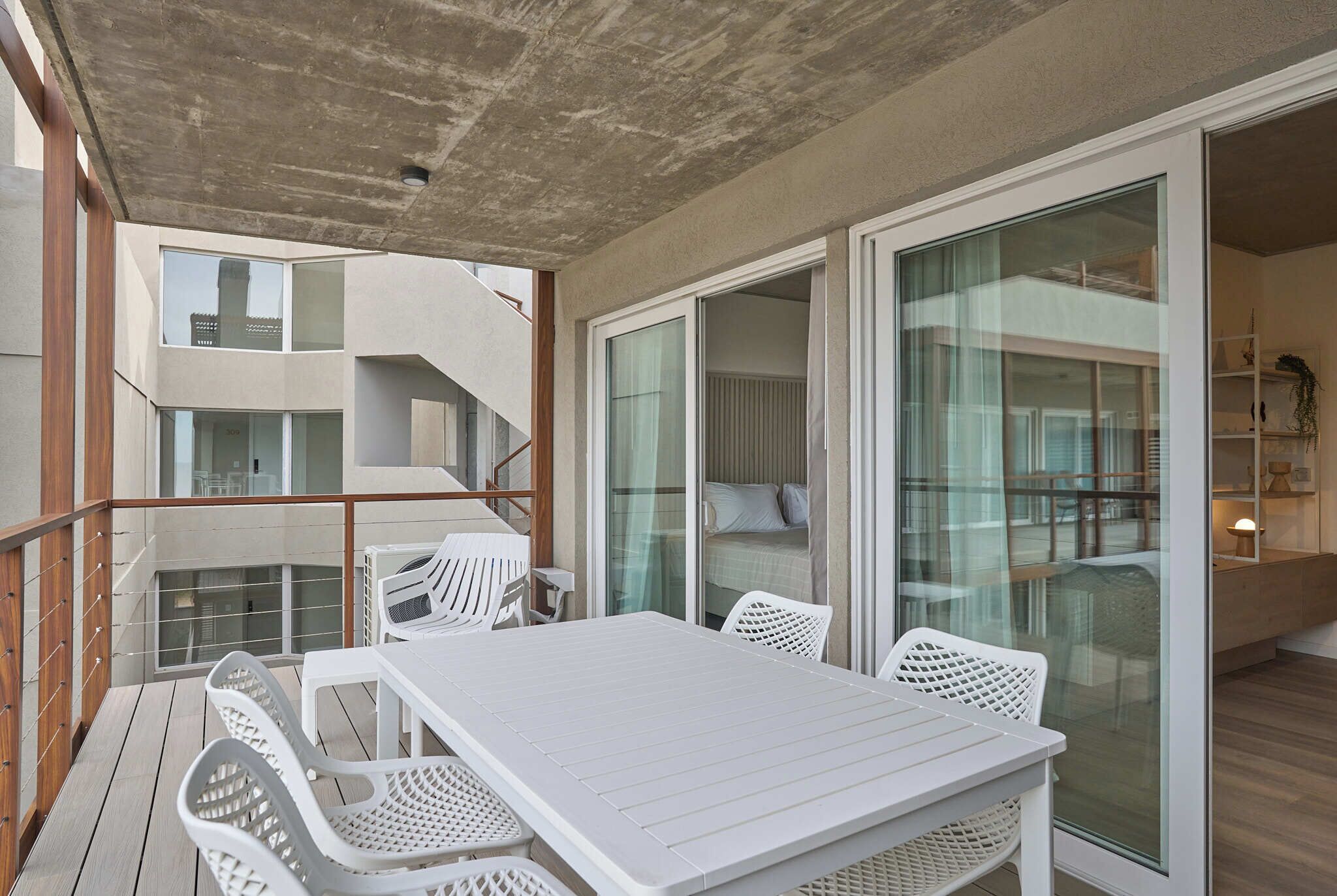 En balkon med et hvidt bord og stole, et trægelænder og udsigt til bygningens indre.