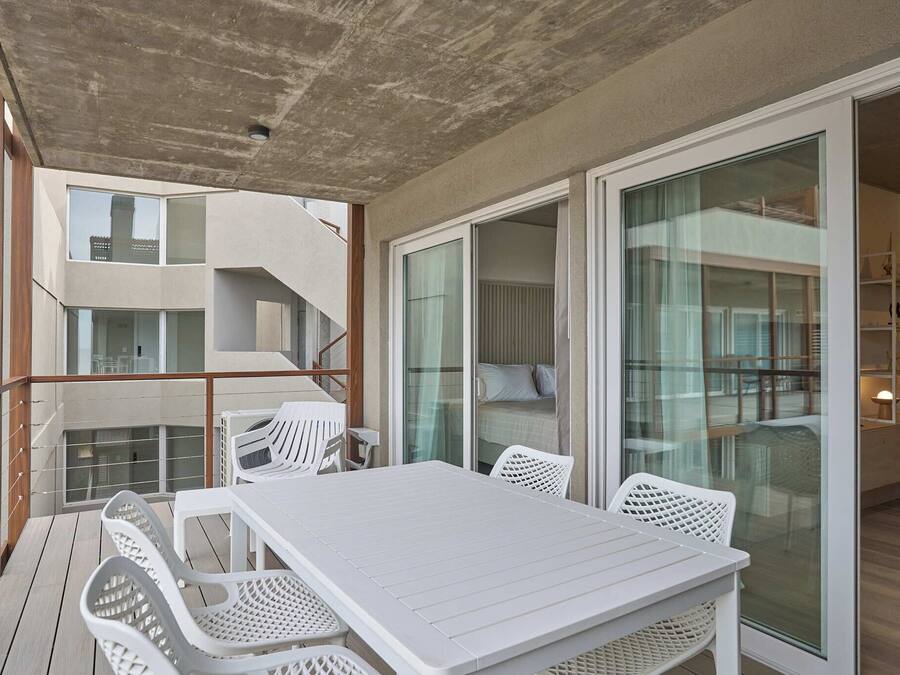 En balkon med et hvidt bord og stole, et trægelænder og udsigt til bygningens indre.