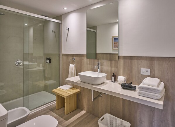 A modern bathroom with a glass-enclosed shower, a large white sink, and a wooden vanity. - Almarena La Reserva (Costa del Este)