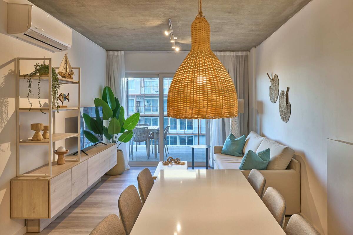 A modern living room with a dining table, sofa, and large windows.