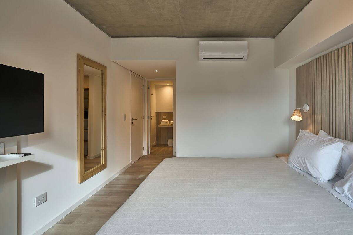 A modern hotel room with a large bed, a flat-screen TV, a wooden wardrobe, and a walk-in closet.