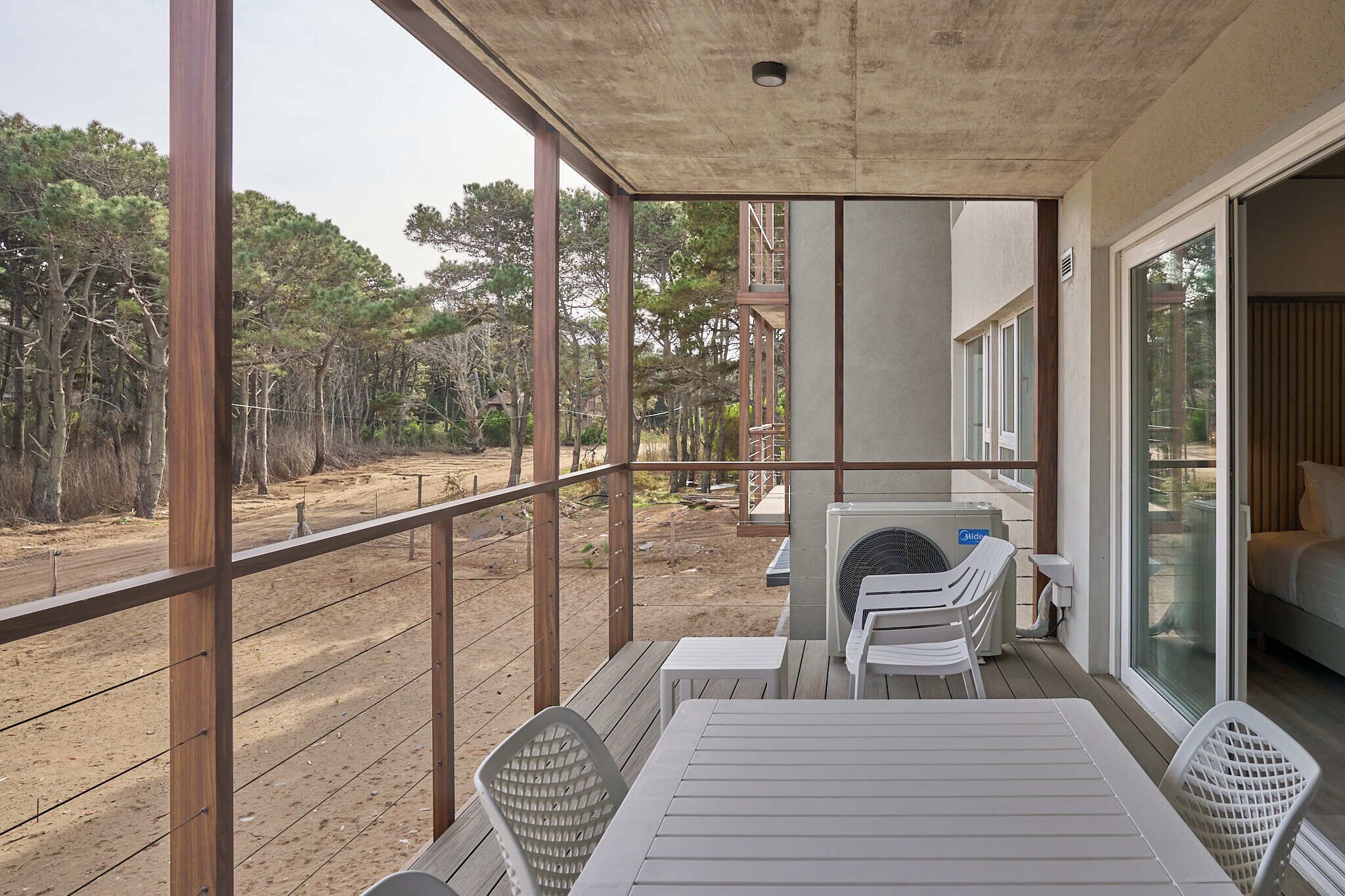 A covered outdoor area with a table and chairs, a view of the surrounding forest, and a building with large windows.