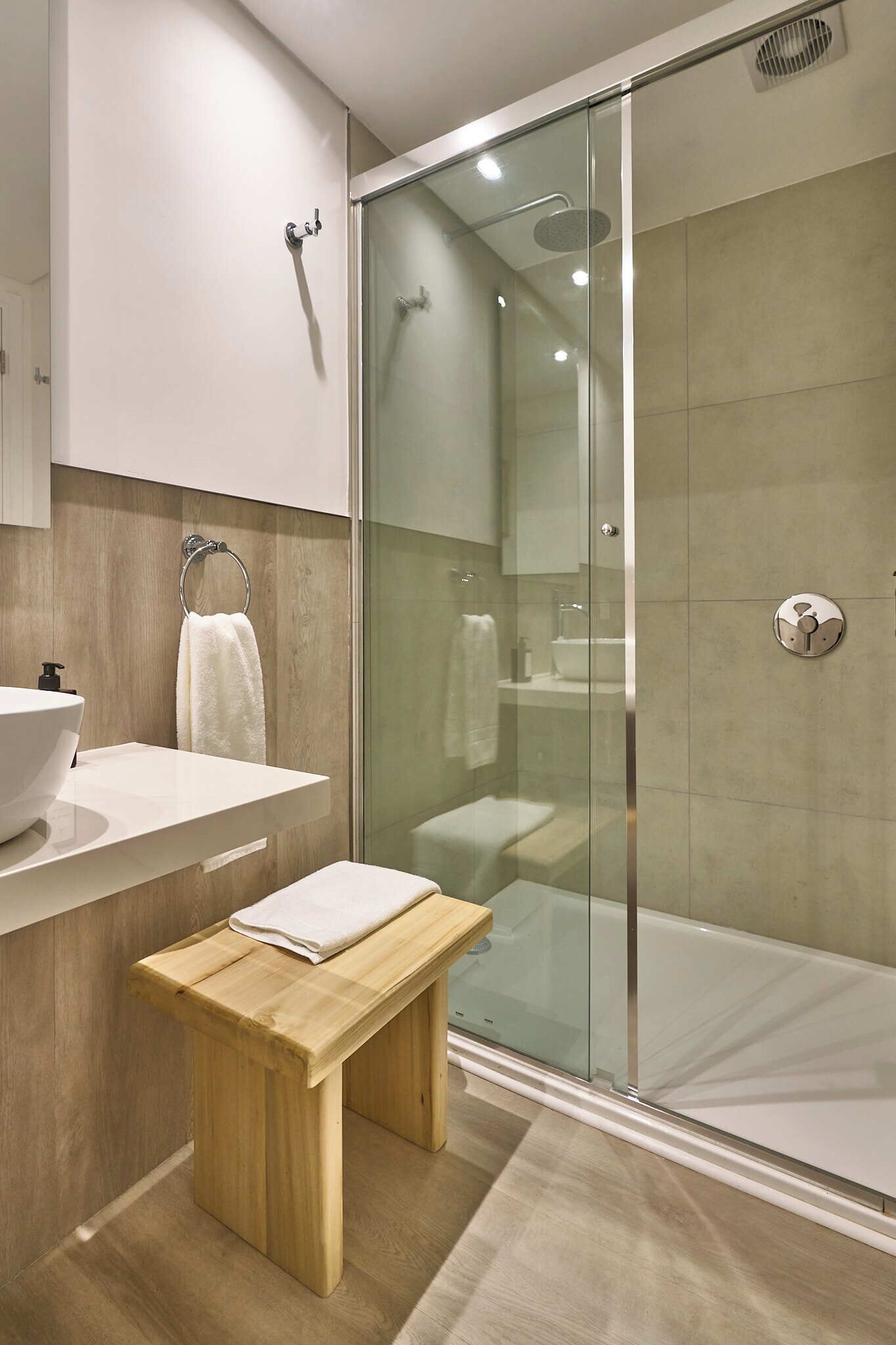 Une salle de bain moderne avec une douche à parois de verre, un banc en bois et un lavabo blanc.