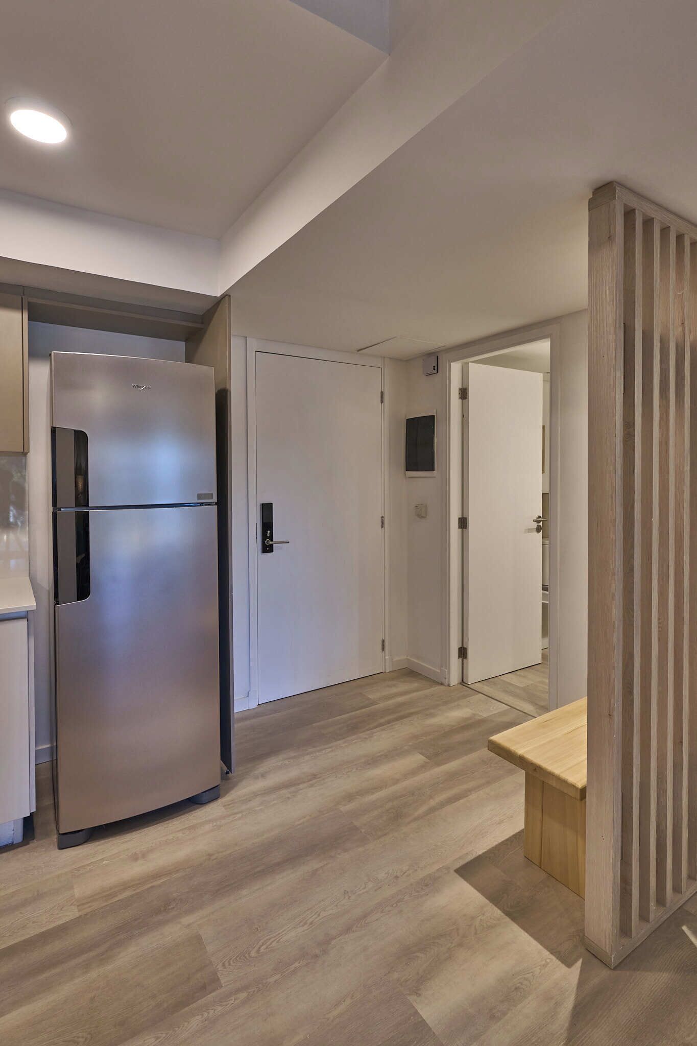 A modern kitchen with a stainless steel refrigerator, wooden flooring, and a bench.