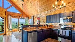 A modern kitchen with wooden walls, a large island, stainless steel appliances, and a view of the mountains. - Epic Views! + Hot Tub + 2 Kings + PS5 + Fire Pit (Sevierville)
