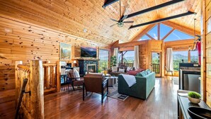 A spacious wooden cabin with a fireplace, a sofa, a dining area, and a kitchen. - Epic Views! + Hot Tub + 2 Kings + PS5 + Fire Pit (Sevierville)