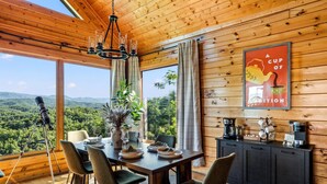 A wooden interior with a dining table set for four, a telescope, and a scenic view through large windows. - Epic Views! + Hot Tub + 2 Kings + PS5 + Fire Pit (Sevierville)