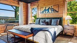 A wooden cabin bedroom with a bed, bench, nightstands, and artwork. - Epic Views! + Hot Tub + 2 Kings + PS5 + Fire Pit (Sevierville)