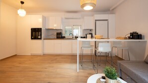 A modern kitchen with white cabinets, a central island with stools, and a hanging light fixture. - The Secret Garden Stay (Agia Paraskevi)