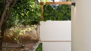 A narrow pathway with a wooden pergola and lush greenery on one side, leading to a white brick wall and a wooden deck on the other. - The Secret Garden Stay (Agia Paraskevi)