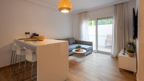 A modern living room with a sofa, a dining area with chairs, a small round table, and a TV on a stand. - The Secret Garden Stay (Agia Paraskevi)