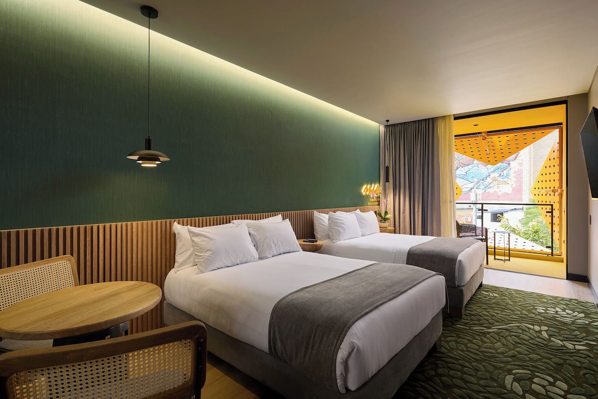 A hotel room with two beds, a small round table, and a balcony with a view.