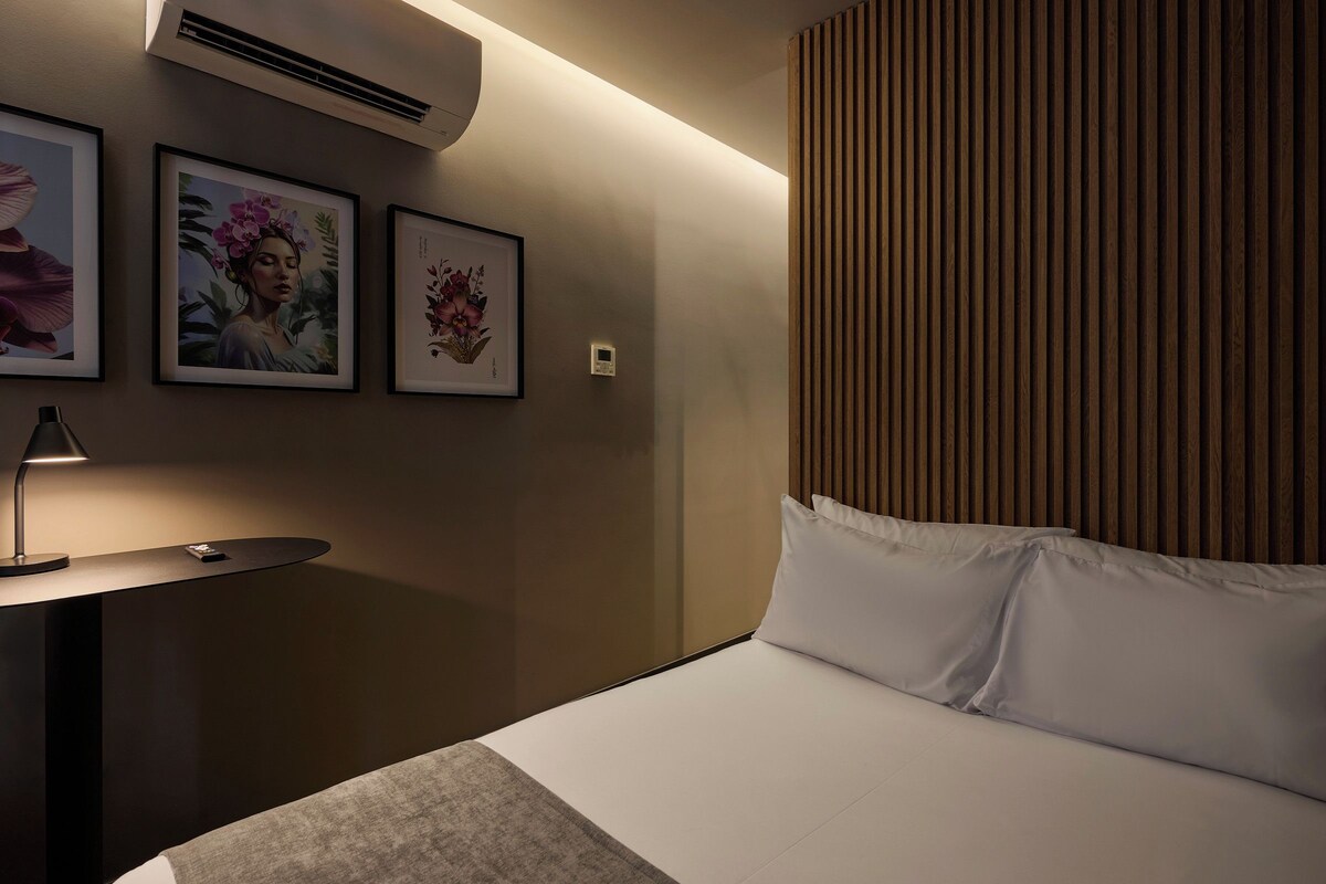 A hotel room with a bed, a bedside table with a lamp, and framed artwork on the wall.