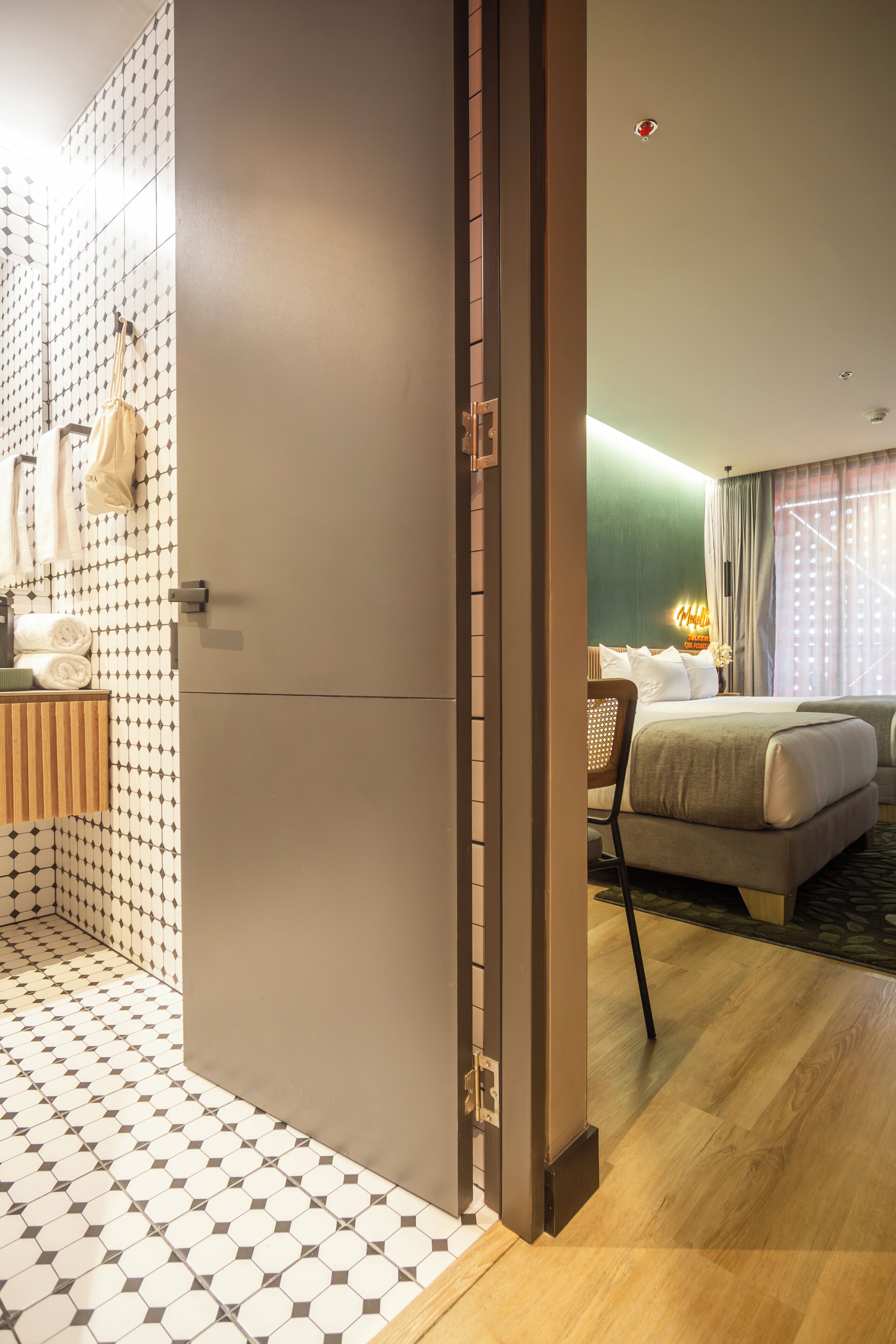 A hotel room with a modern design, featuring a large bed, a seating area, and a bathroom with a patterned tile floor.